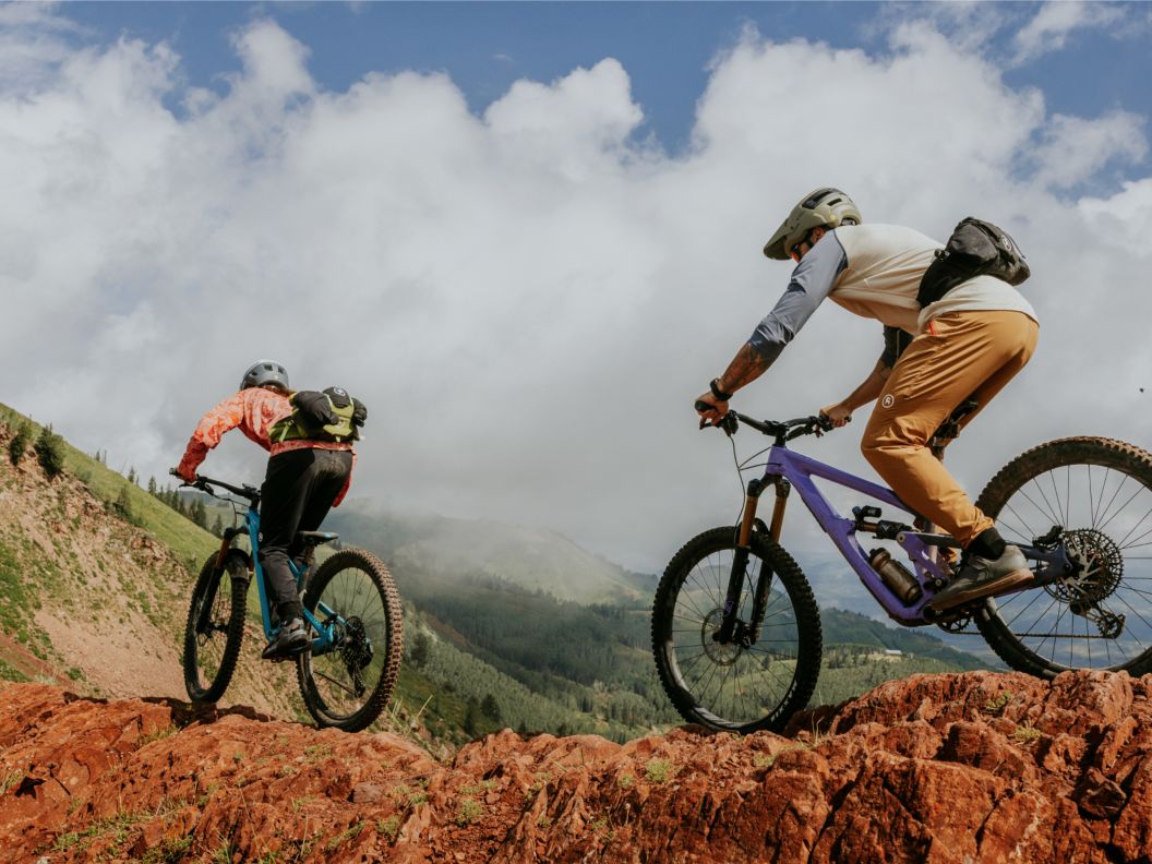 Two bikers ride across a rocky ridgeline.